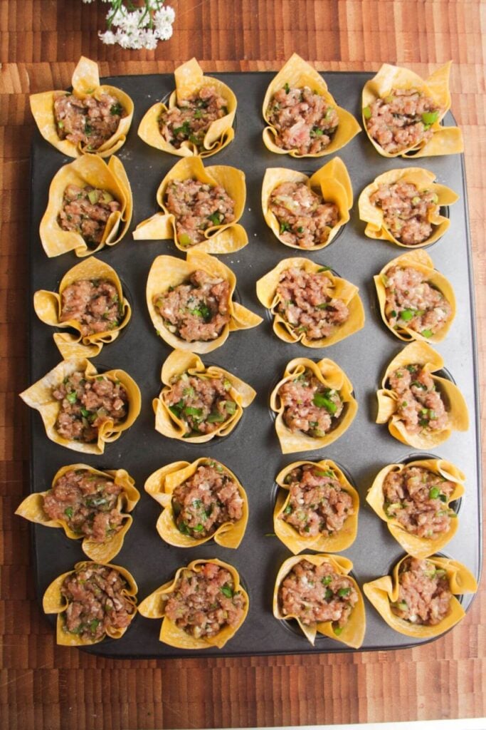 Dumpling filling in wonton cups in a mini muffin tin.