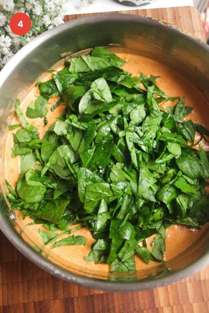 Spinach added to chickpea coconut curry in a pan.