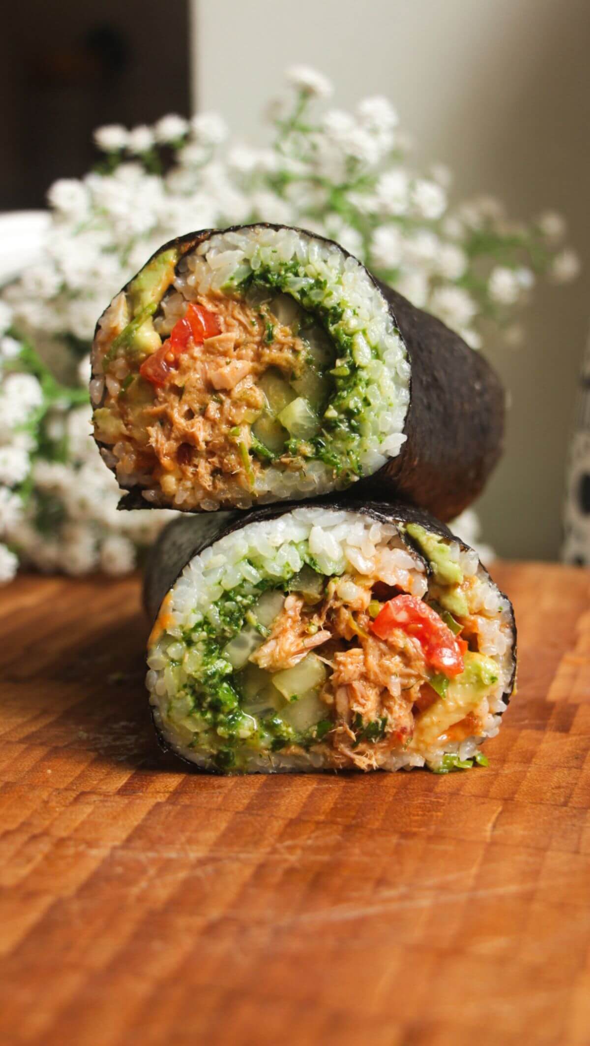 Sliced tuna sushi burrito on top of eachother on a wooden board.
