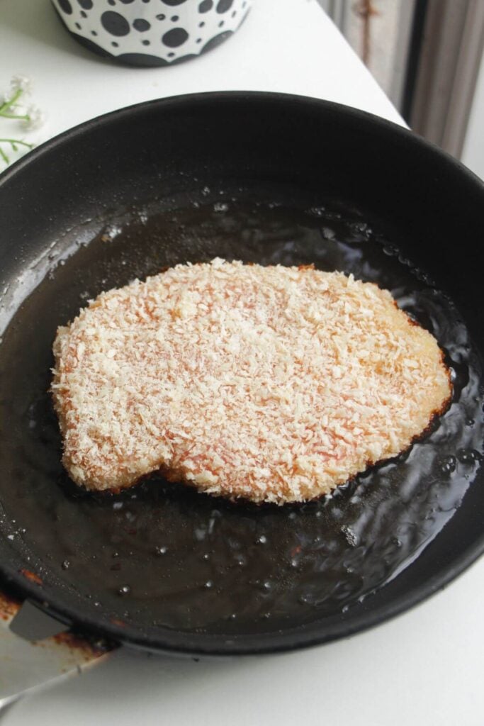Breaded chicken breast in a small pan.