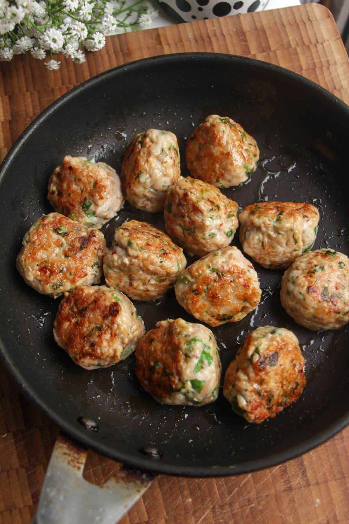 Chicken meatballs browned in a small pan.
