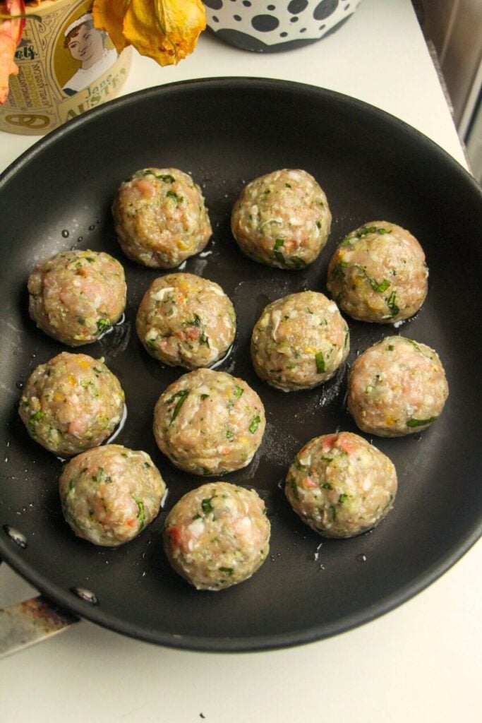 Chicken and pesto meatballs browning in a large pan.