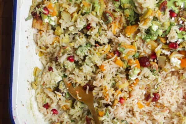 Spoon in baked rice topped with feta, pomegranate seeds and green tahini sauce.