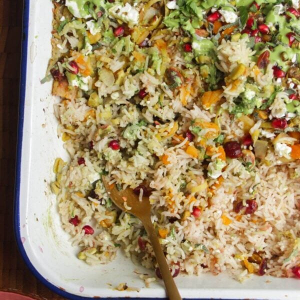 Spoon in baked rice topped with feta, pomegranate seeds and green tahini sauce.