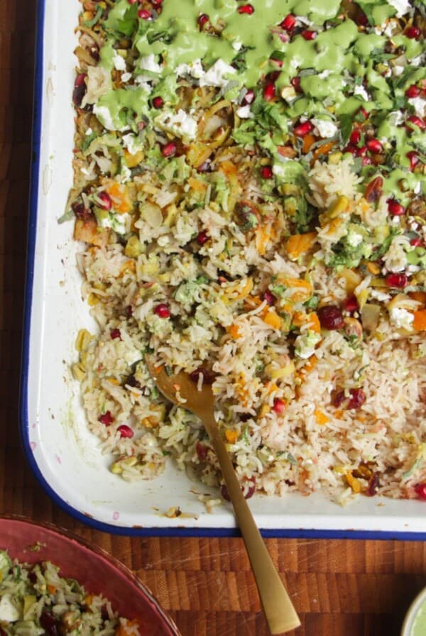 Spoon in baked rice topped with feta, pomegranate seeds and green tahini sauce.