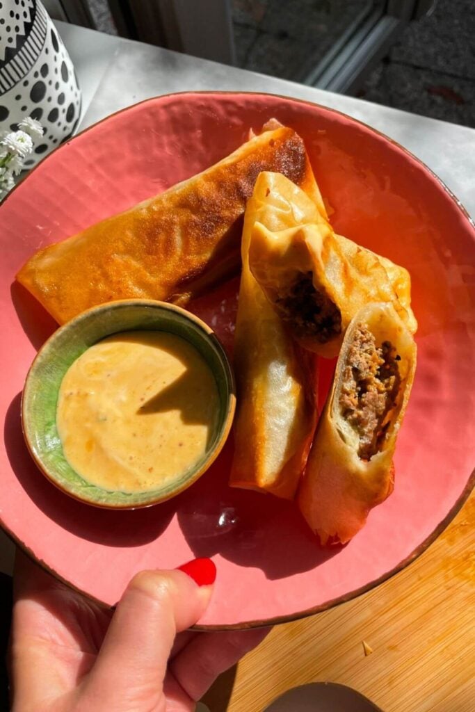 Three cheeseburger spring rolls in a pink plate.