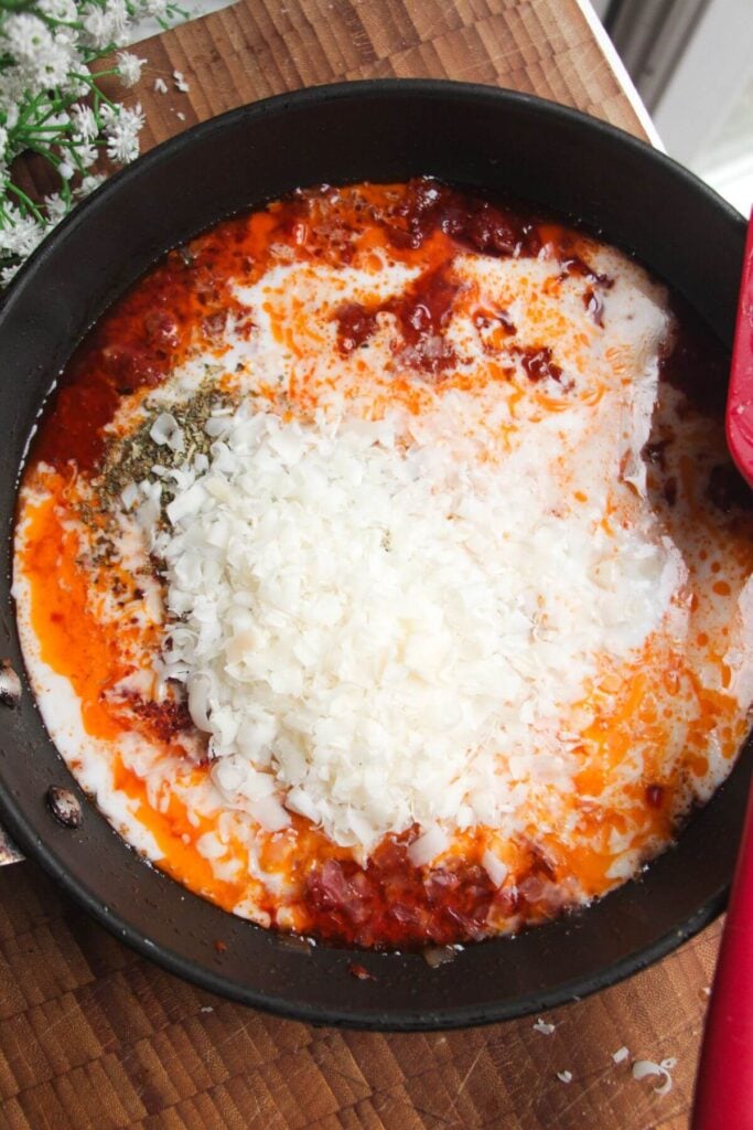 Grated parmesan added to sauce in a small pan.