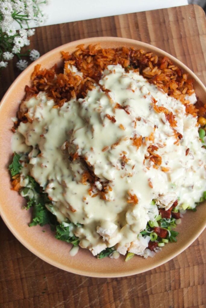 Caesar dressing poured over crispy rice salad in pink bowl.