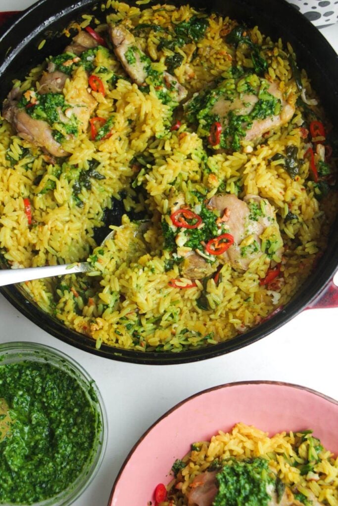 Pesto topped chicken with rice in a large pot with pink plate and pesto on the side.