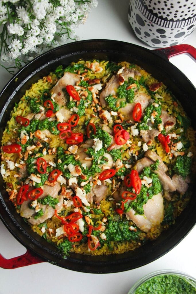Pesto topped golden chicke and rice in a large pot.