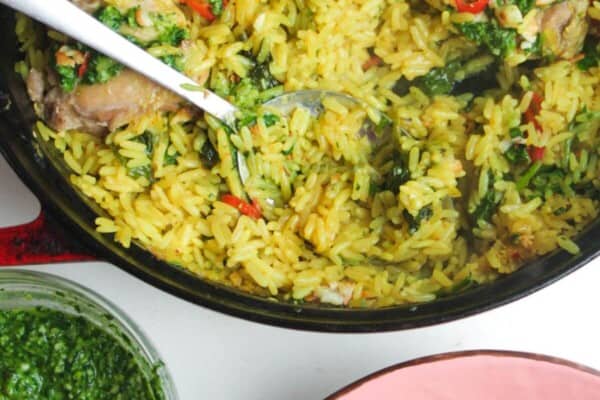 Pesto topped chicken with rice in a large pot with pink plate and pesto on the side.