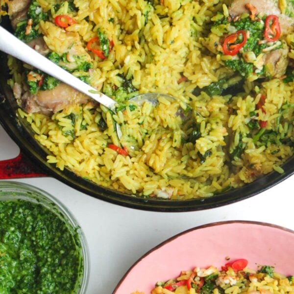 Pesto topped chicken with rice in a large pot with pink plate and pesto on the side.