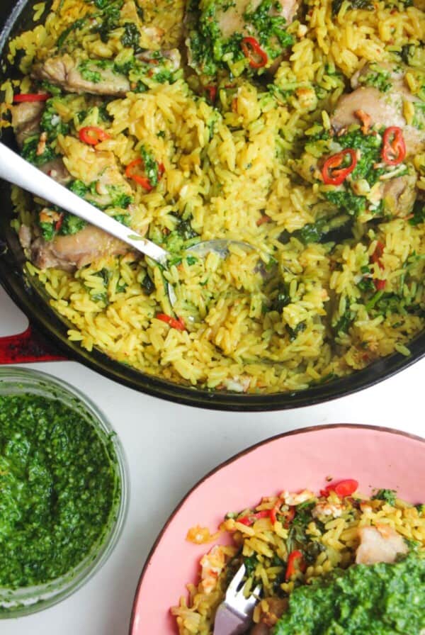 Pesto topped chicken with rice in a large pot with pink plate and pesto on the side.