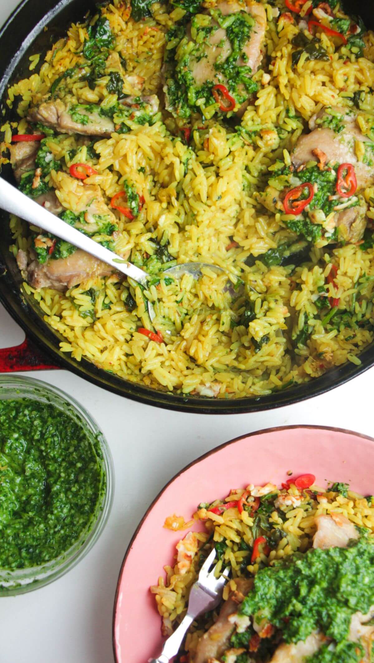 Pesto topped chicken with rice in a large pot with pink plate and pesto on the side.