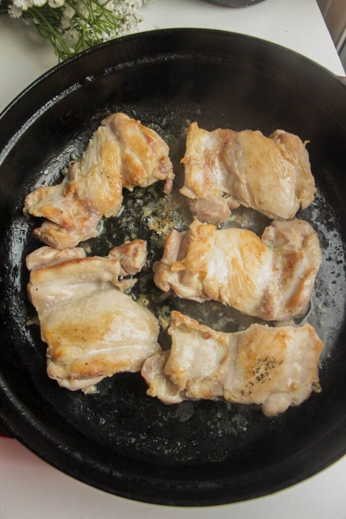 Chicken thighs cooking in a large pan.
