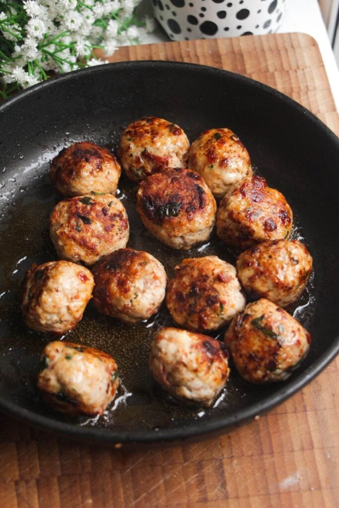 Browned chicken meatballs in a black pan.