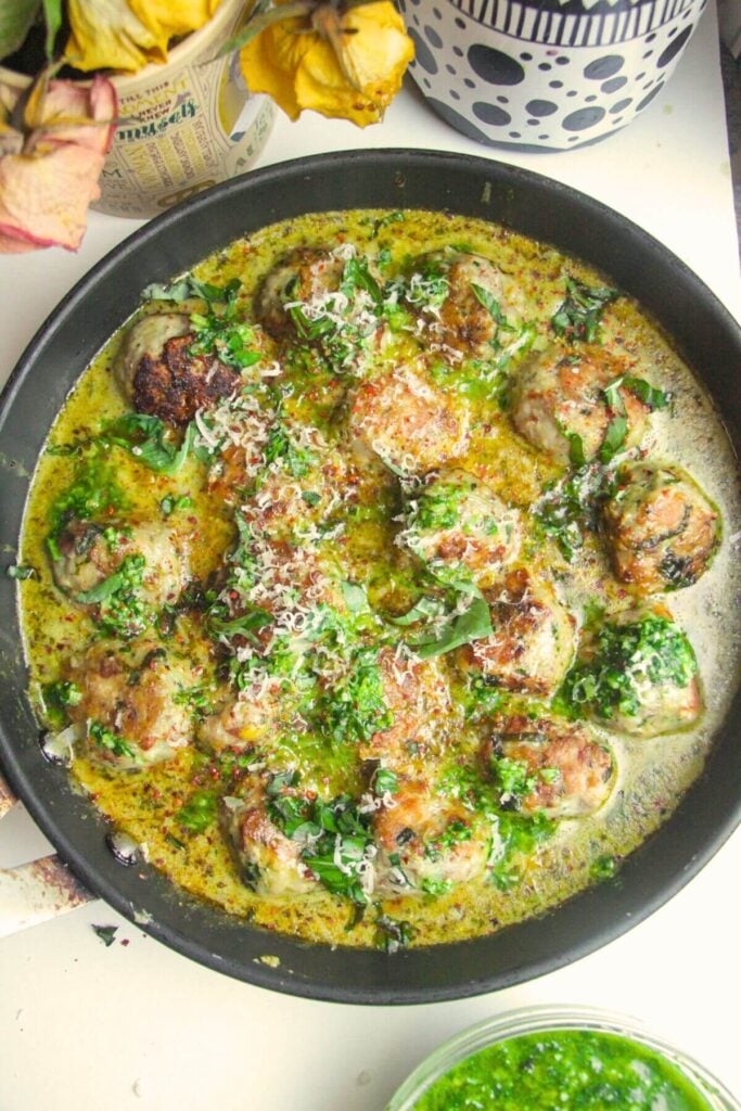 Chicken pesto meatballs in a creamy green pesto sauce in a large pan.