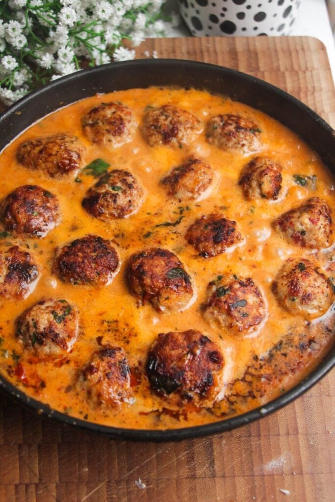 Browned meatballs simmering in 'Marry Me' sauce in a pan.