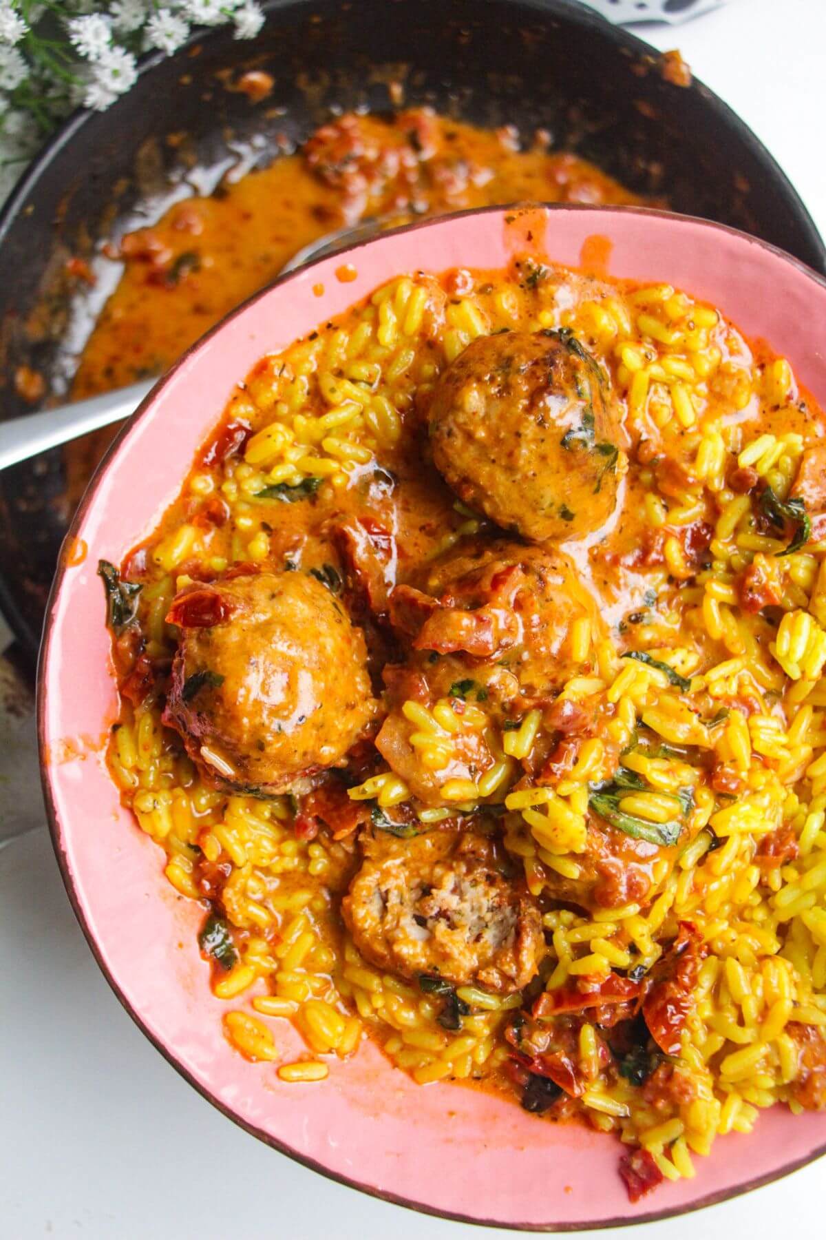 'Marry Me' chicken meatballs on golden rice in a pink plate.
