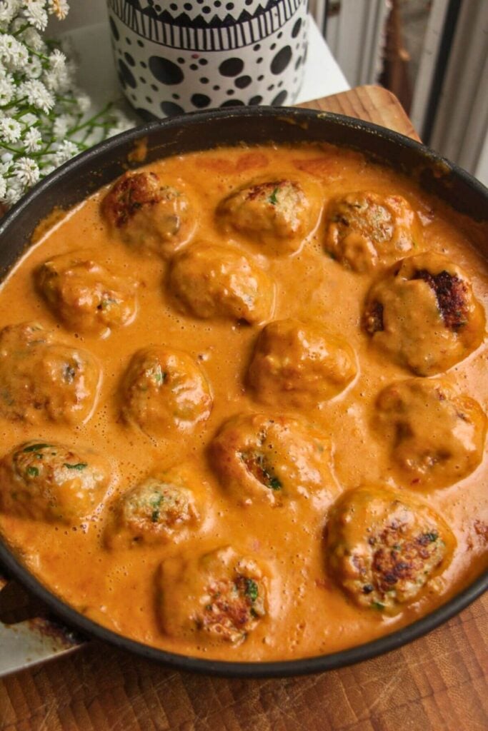Chicken meatballs simmering in a satay sauce.