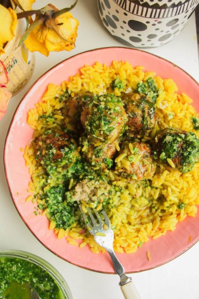 Chicken and pesto meatballs on top of golden rice with pesto on top.