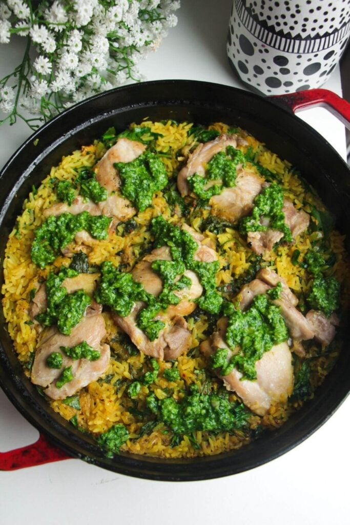 Pesto dolloped on top of golden chicken thighs in a large pan.