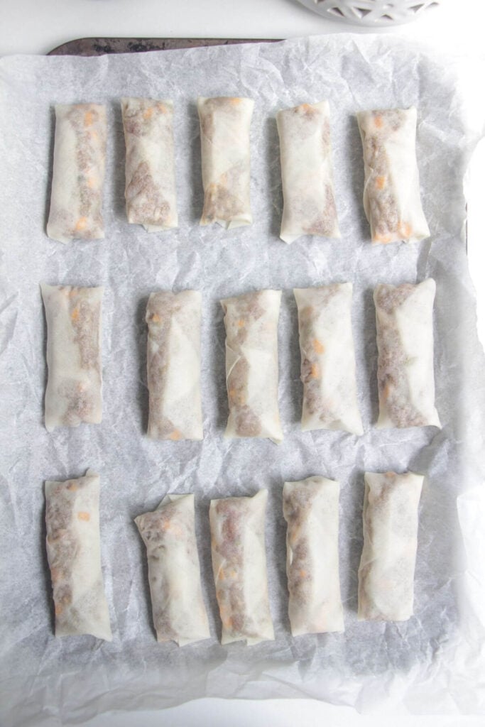 Cheeseburger spring rolls on a lined oven tray.
