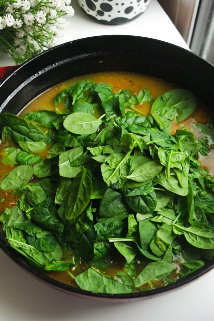 Baby spinach leaves added to rice and stock in large pan.