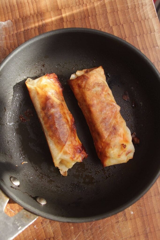 Cheeseburger spring rolls crisped up in frying pan.