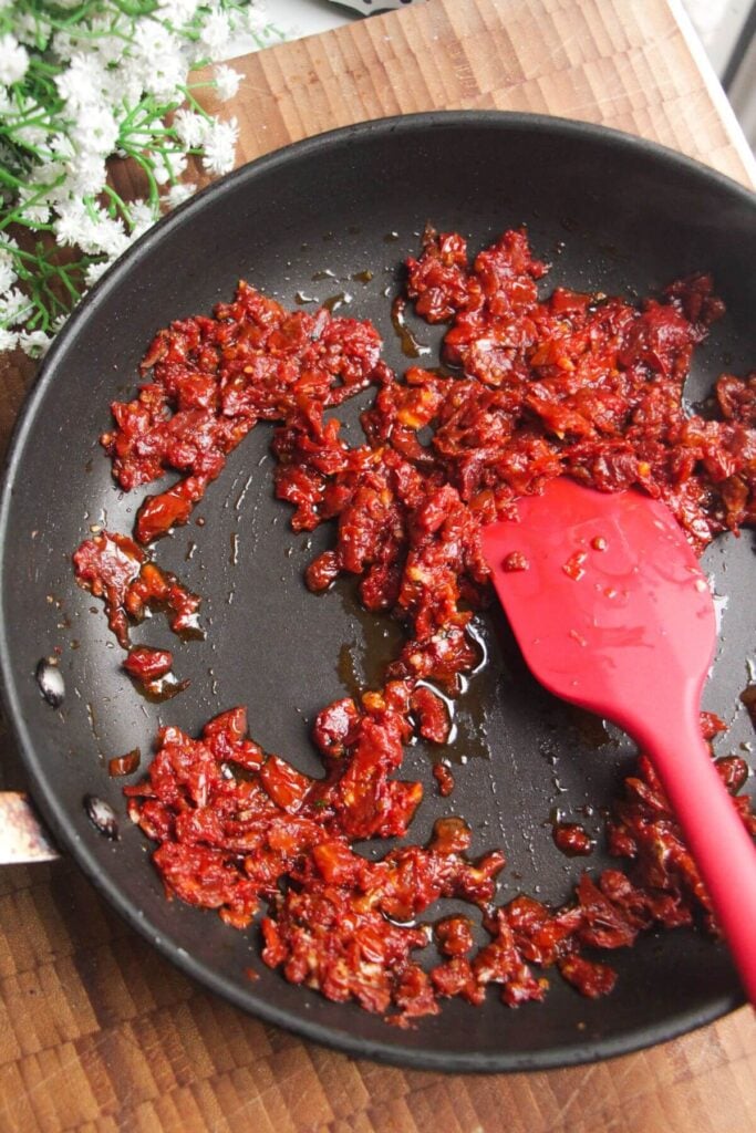 Stirring sundried tomatoes and garlic in a pan.