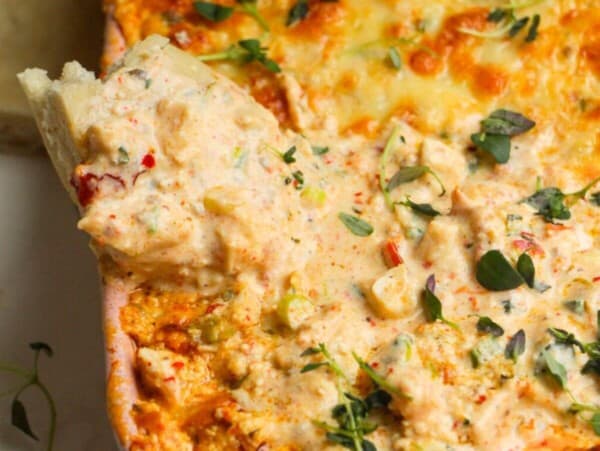 Pita bread dipped into baked dip in a baking dish.