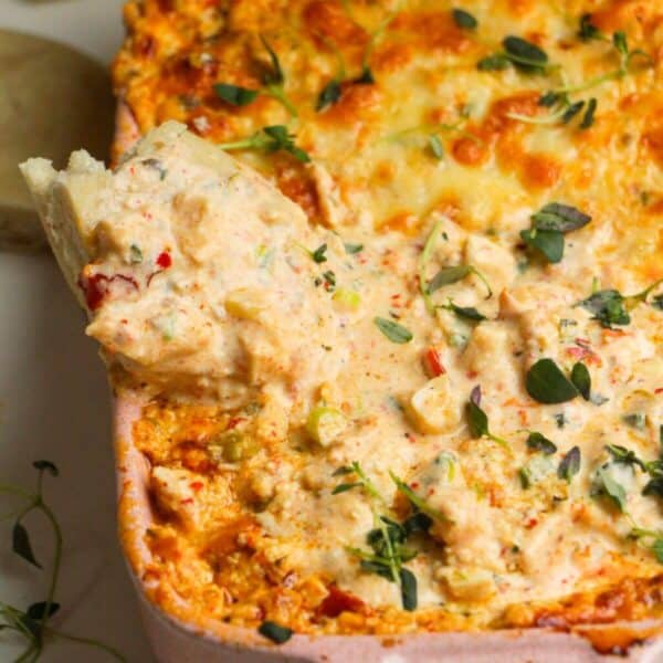 Pita bread dipped into baked dip in a baking dish.