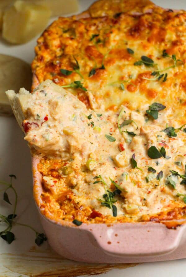 Pita bread dipped into baked dip in a baking dish.