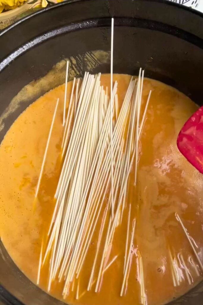 Noodles added to coconut peanut sauce in a pot.