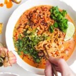 Hand with chopsticks with a bowl of peanut butter noodles.