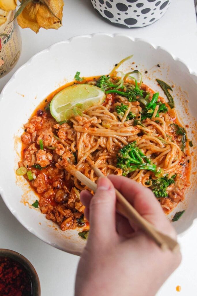 Hand with chopsticks with a bowl of peanut butter noodles.