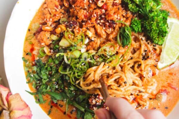 Hand with chopsticks with a bowl of peanut butter noodles.