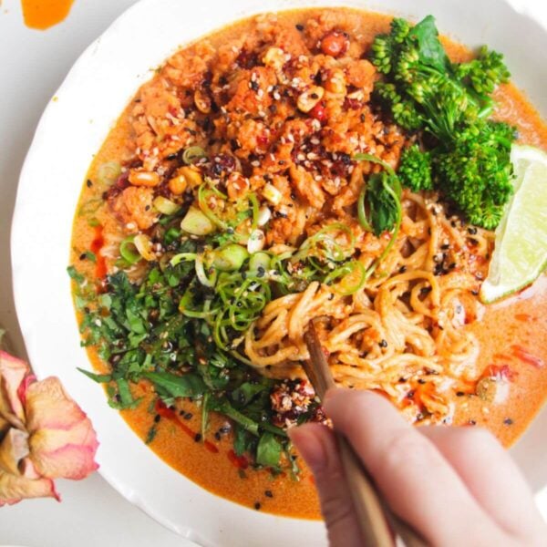 Hand with chopsticks with a bowl of peanut butter noodles.
