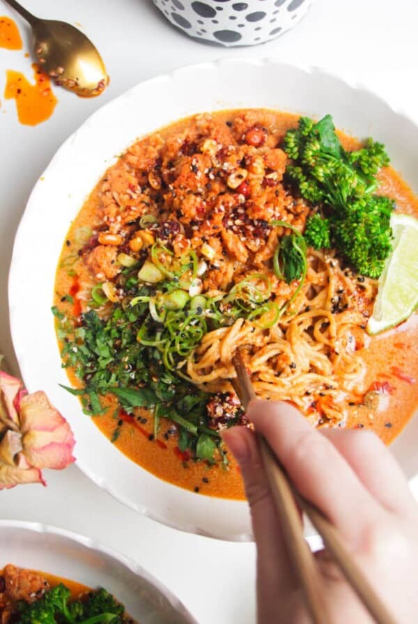 Hand with chopsticks with a bowl of peanut butter noodles.