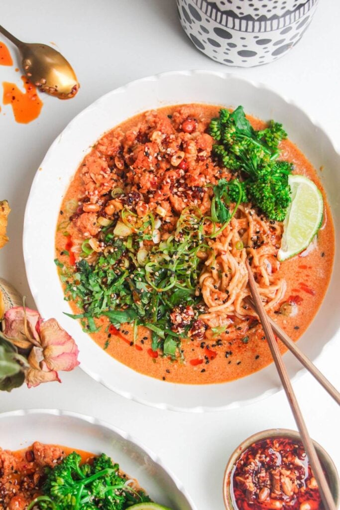 Peanut butter noodles topped with chicken and herbs in a bowl.