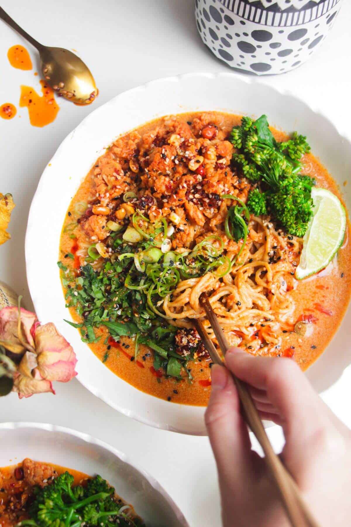 Hand with chopsticks with a bowl of peanut butter noodles.