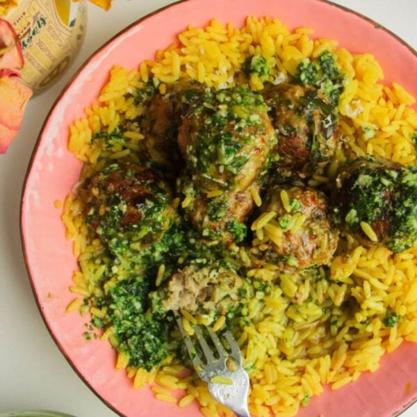 Chicken and pesto meatballs on top of golden rice with pesto on top.