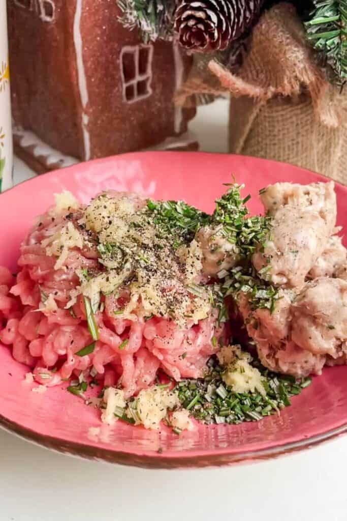 Ground turkey, sausage meat, rosemary and garlic in a bowl.