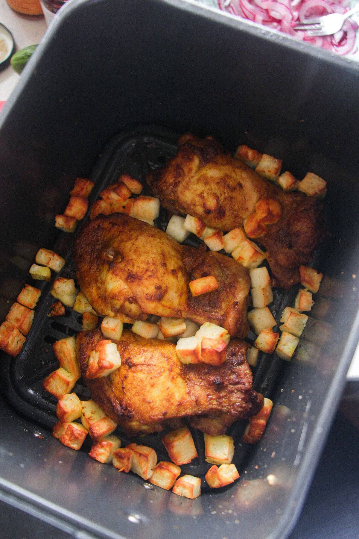 Chicken thighs and halloumi cooked in an air fryer basket.