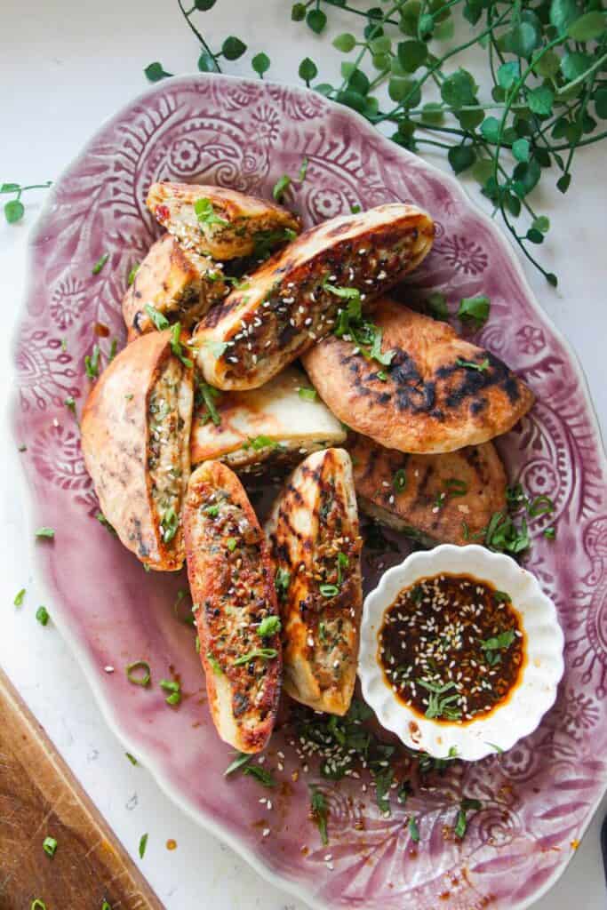 Dumpling stuffed flatbreads on a pink plate with dipping sauce on the side.
