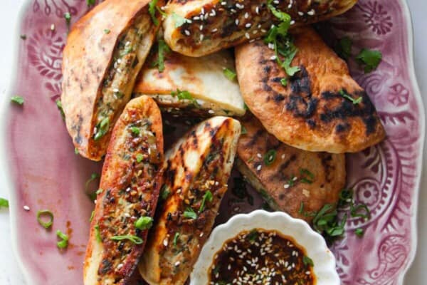 Dumpling stuffed flatbreads on a pink plate with dipping sauce on the side.