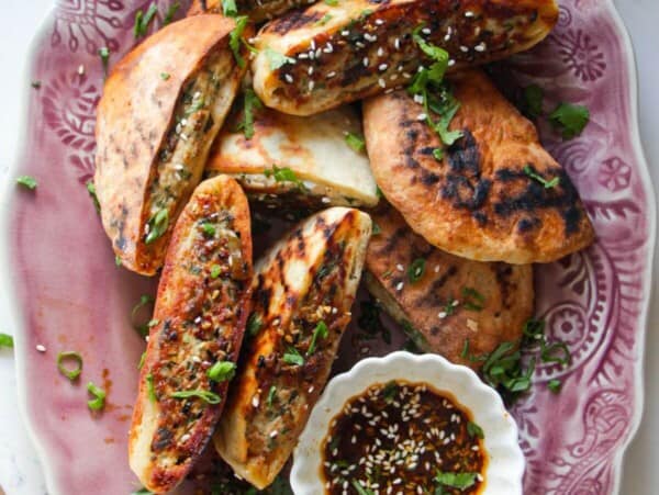 Dumpling stuffed flatbreads on a pink plate with dipping sauce on the side.