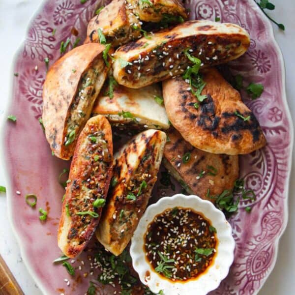 Dumpling stuffed flatbreads on a pink plate with dipping sauce on the side.