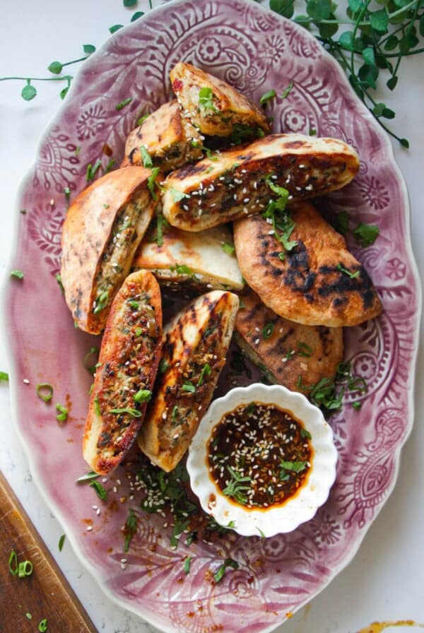Dumpling stuffed flatbreads on a pink plate with dipping sauce on the side.