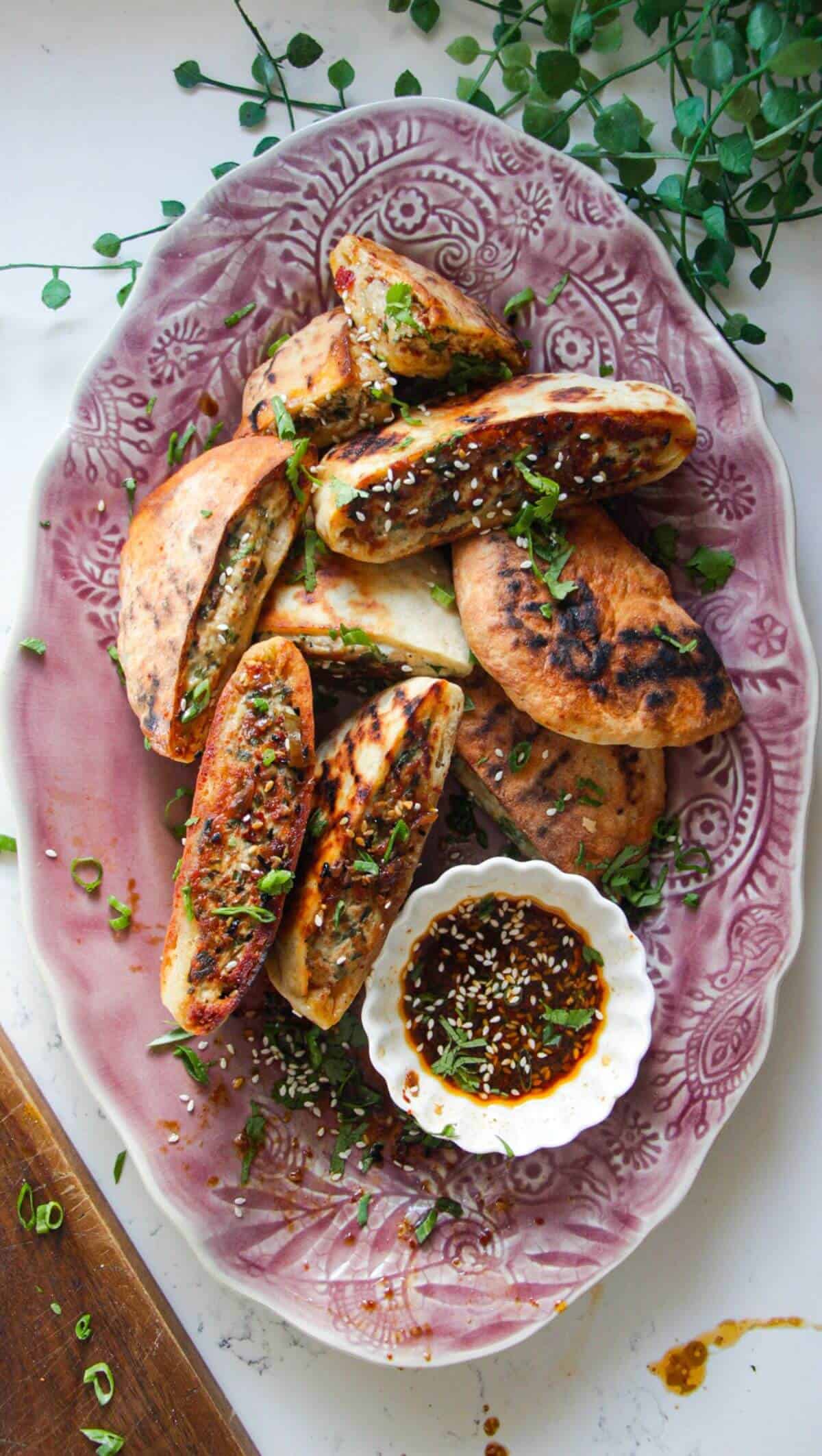 Dumpling stuffed flatbreads on a pink plate with dipping sauce on the side.